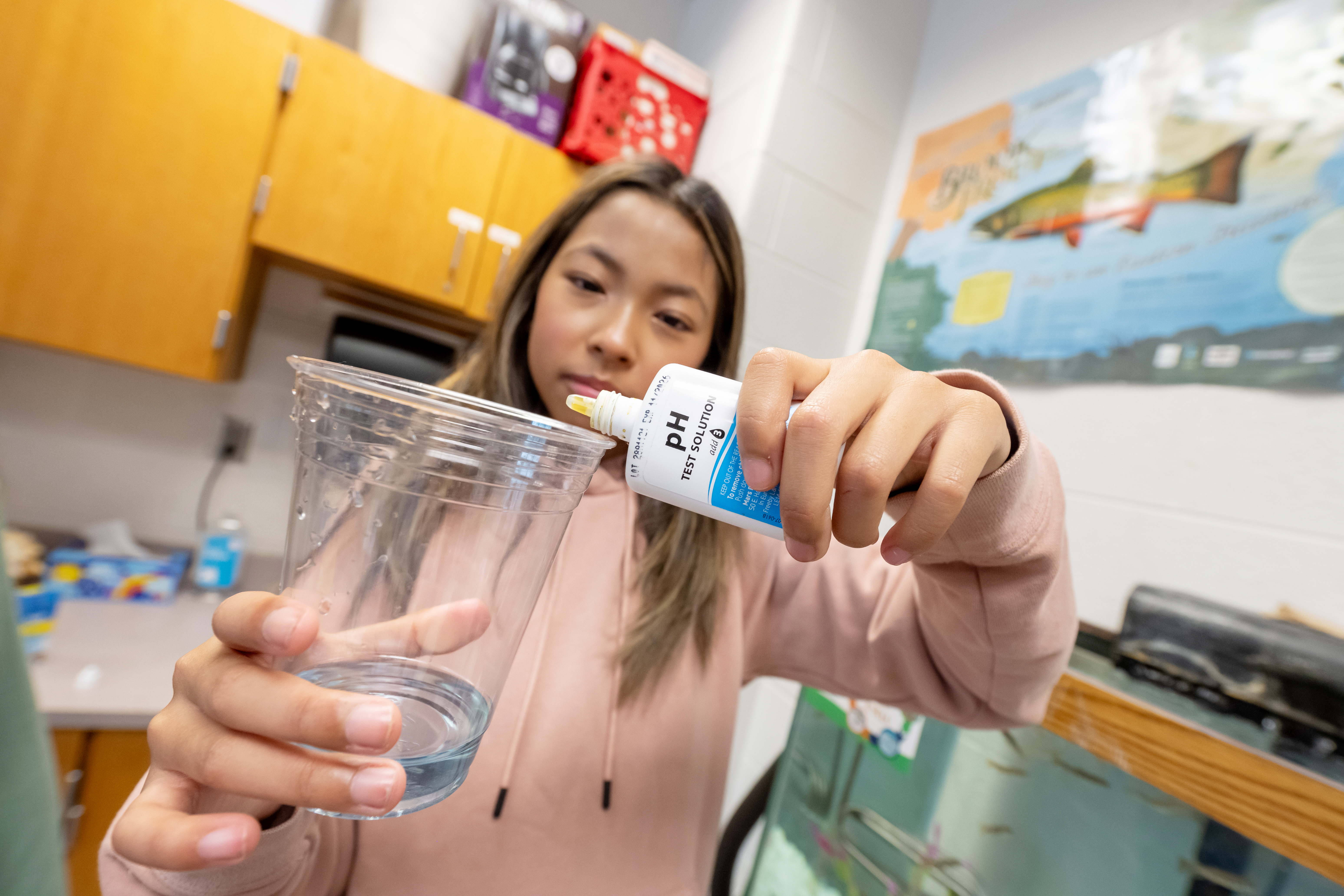 A student drops a pH test solution into a sample of tank water.