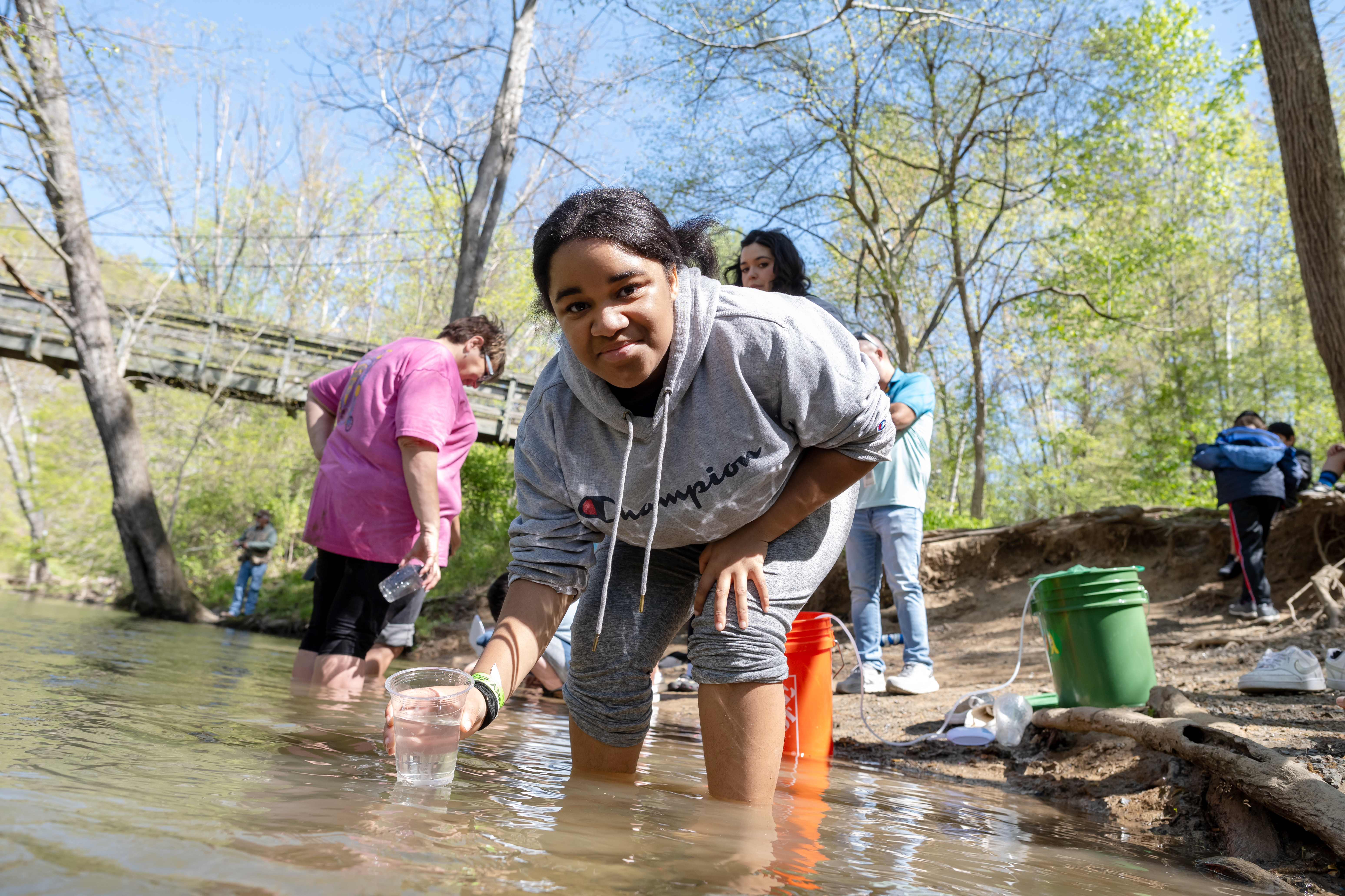 A student smiles as she holds a cup containing a fry in the ankle-deep waters of the stream.