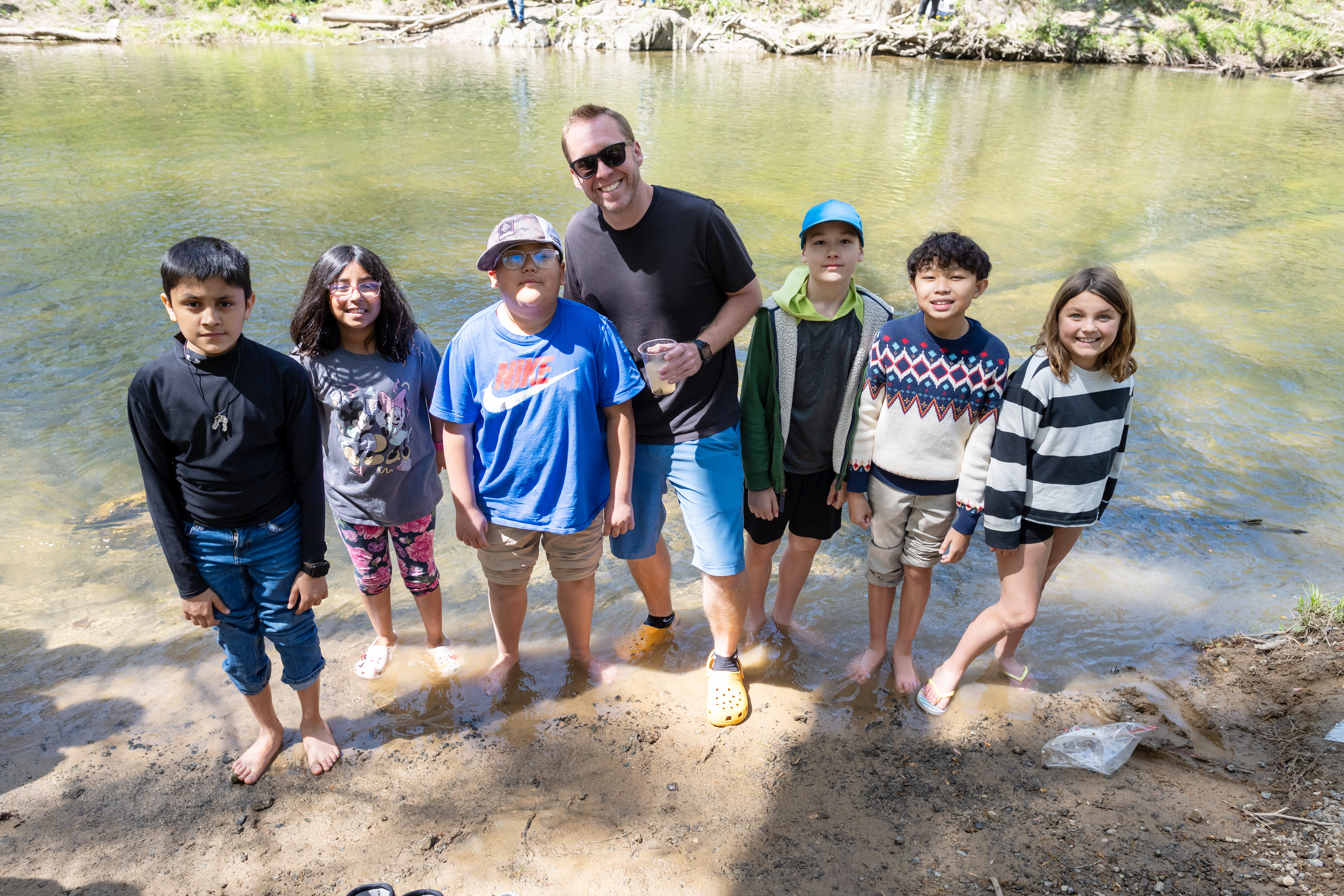 Students smile with Centreville Elementary School principal, Josh Douds, center. Douds holds a fry in a cup as he joins students for the trout release.